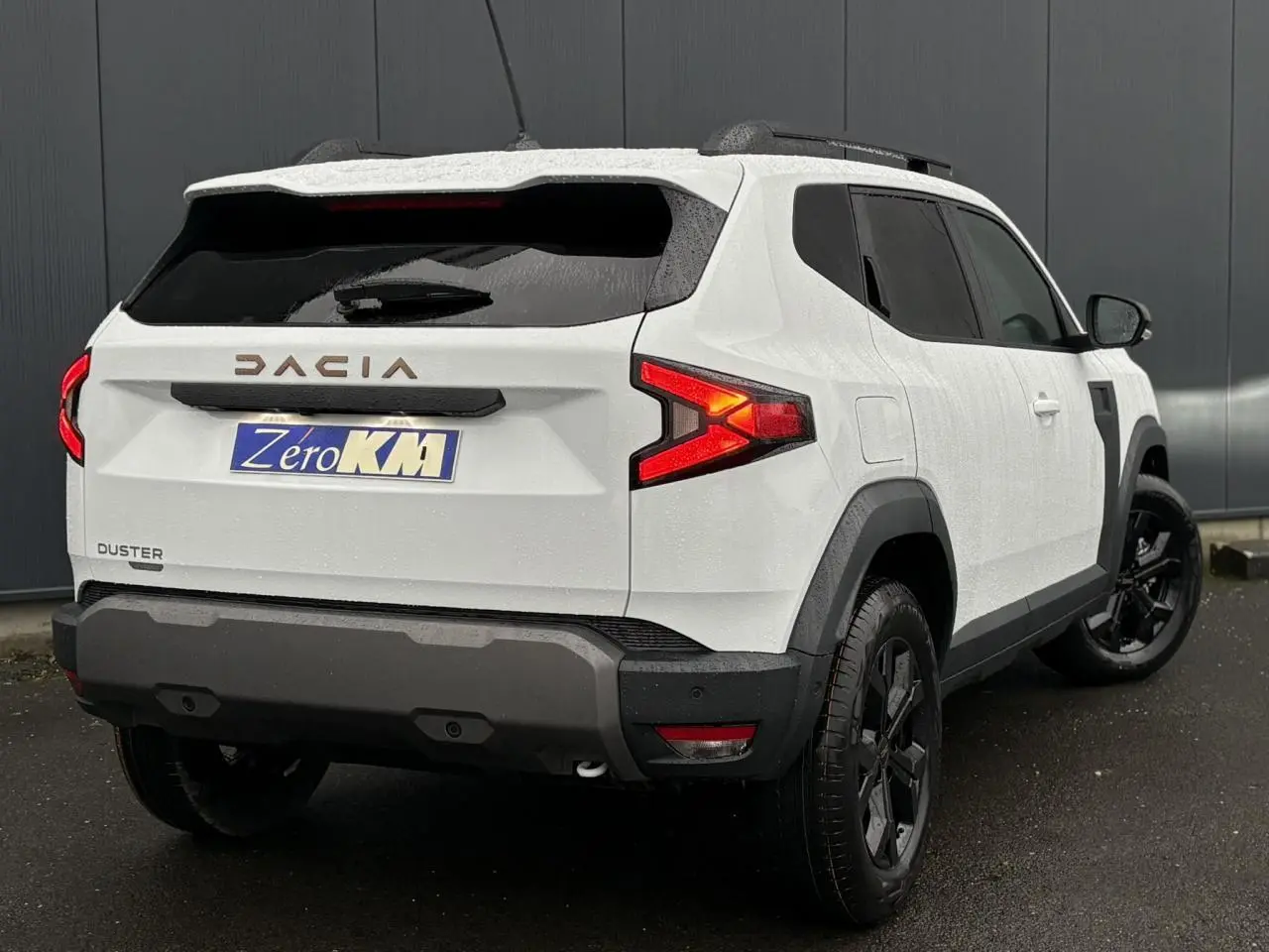 Vue 3/4 arrière droite du Dacia Duster blanc Glacier avec jantes noires et barres de toit noires.