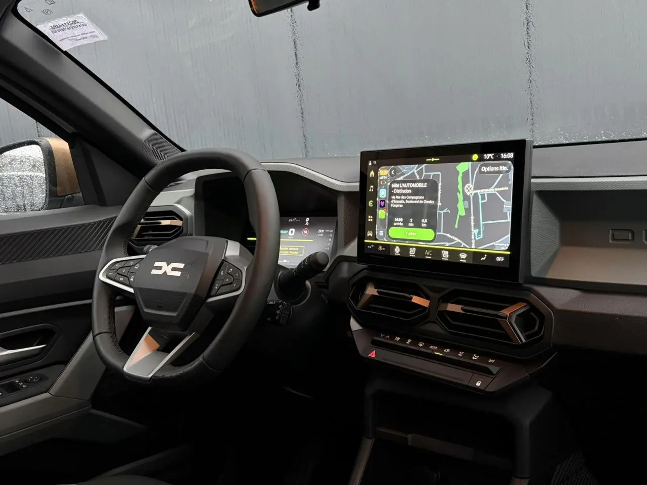 Vue intérieure côté conducteur du Dacia Duster 2026 avec volant noir, écran tactile central et détails brun cuivré.