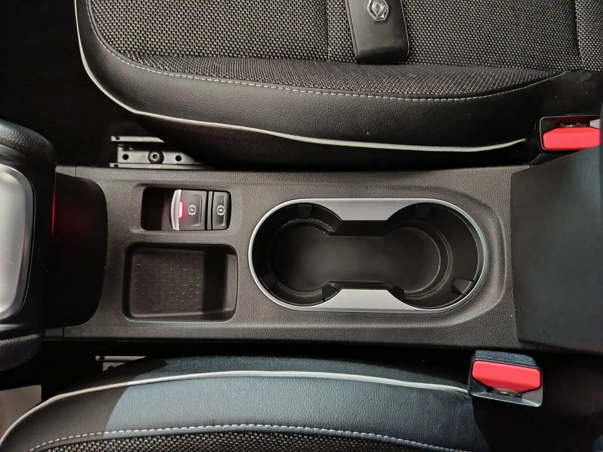 Vue plongeante sur la console centrale noire du Renault Captur rouge 2024, avec porte-gobelets et bouton frein électrique.