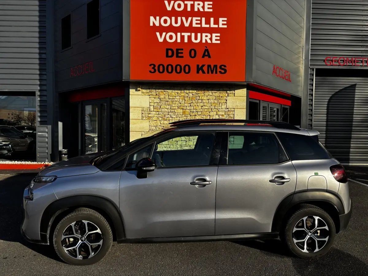 Profil côté gauche du Citroën C3 Aircross gris clair 2024, avec jantes alliage et toit noir contrasté visible.
