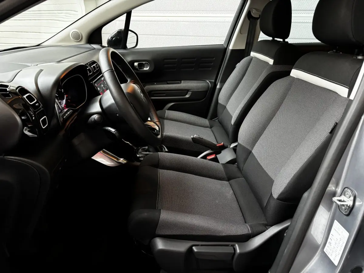 Intérieur côté conducteur du Citroën C3 Aircross gris clair 2024, sièges tissu noir et gris avec tableau de bord moderne.