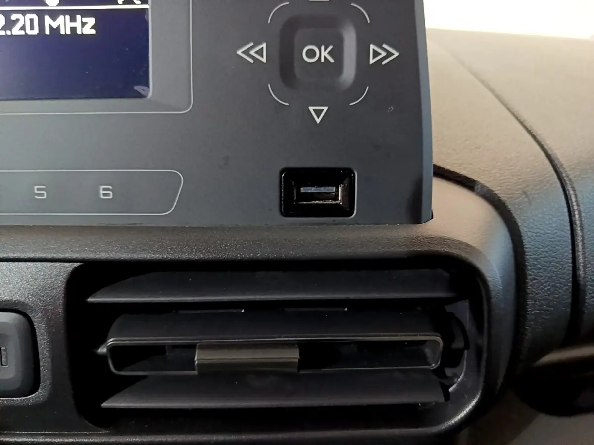 Gros plan sur la console centrale noire du Citroën Berlingo blanc, montrant l'écran radio et une prise USB sous les commandes.