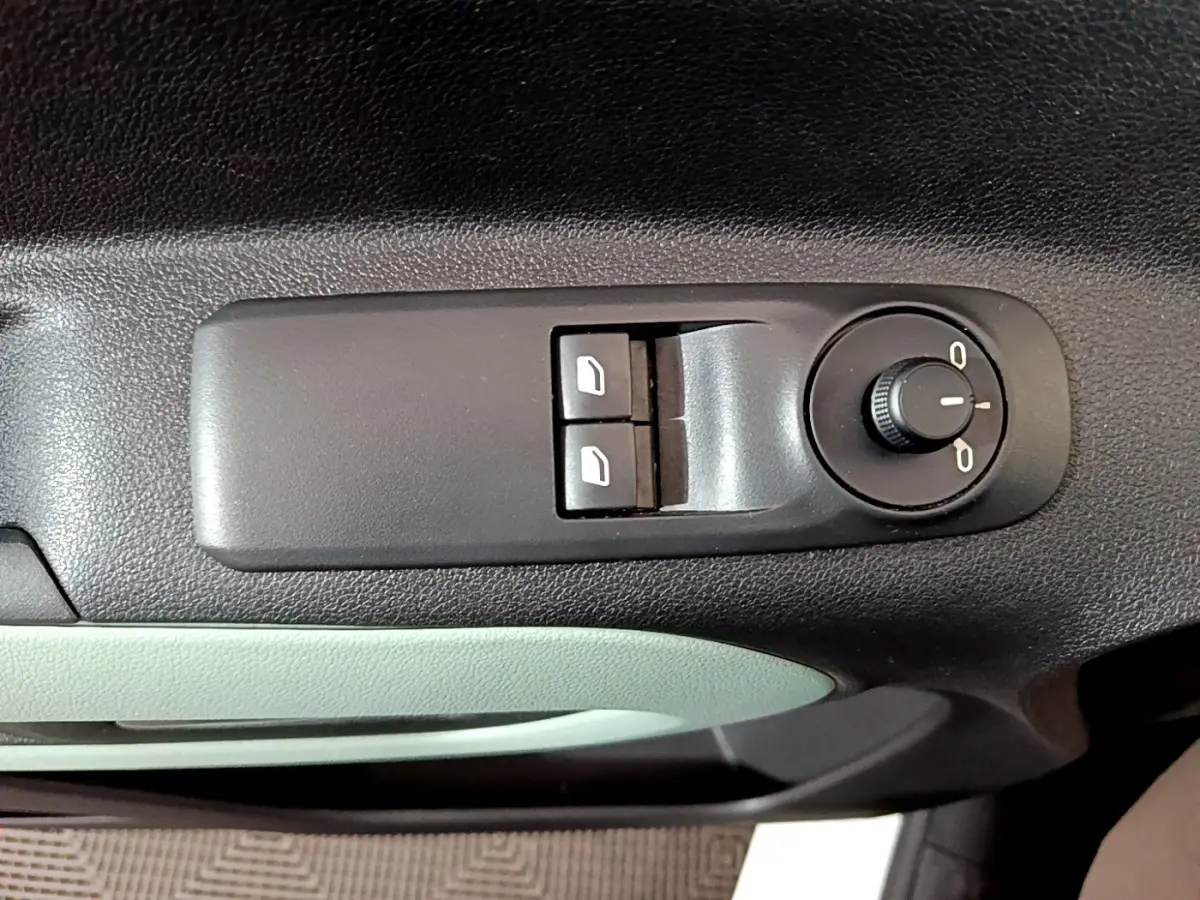 Gros plan sur les commandes de réglage des vitres et des rétroviseurs côté conducteur du Citroën Berlingo blanc, intérieur noir et vert pâle.