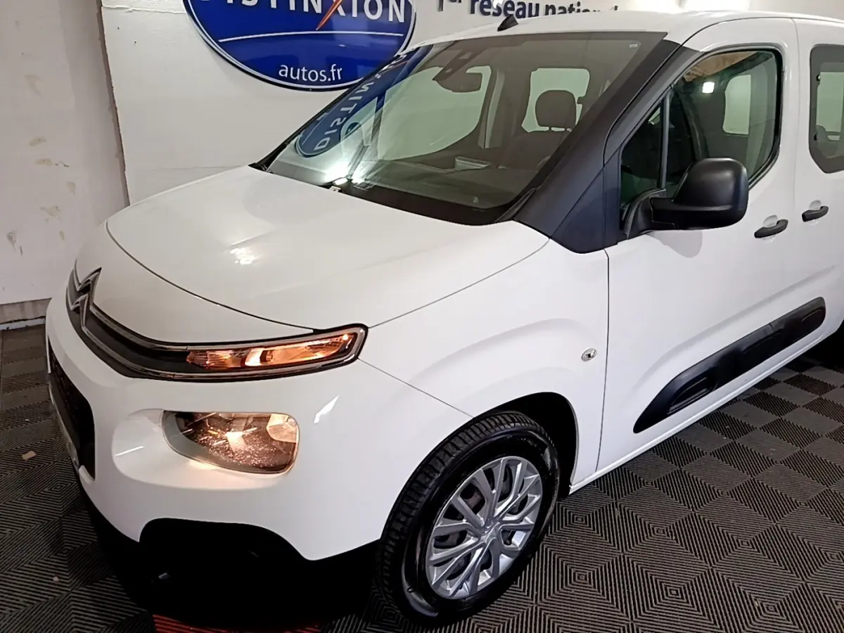 Vue 3/4 avant droit d'un Citroën Berlingo blanc 2019 avec phares allumés et protections latérales noires.