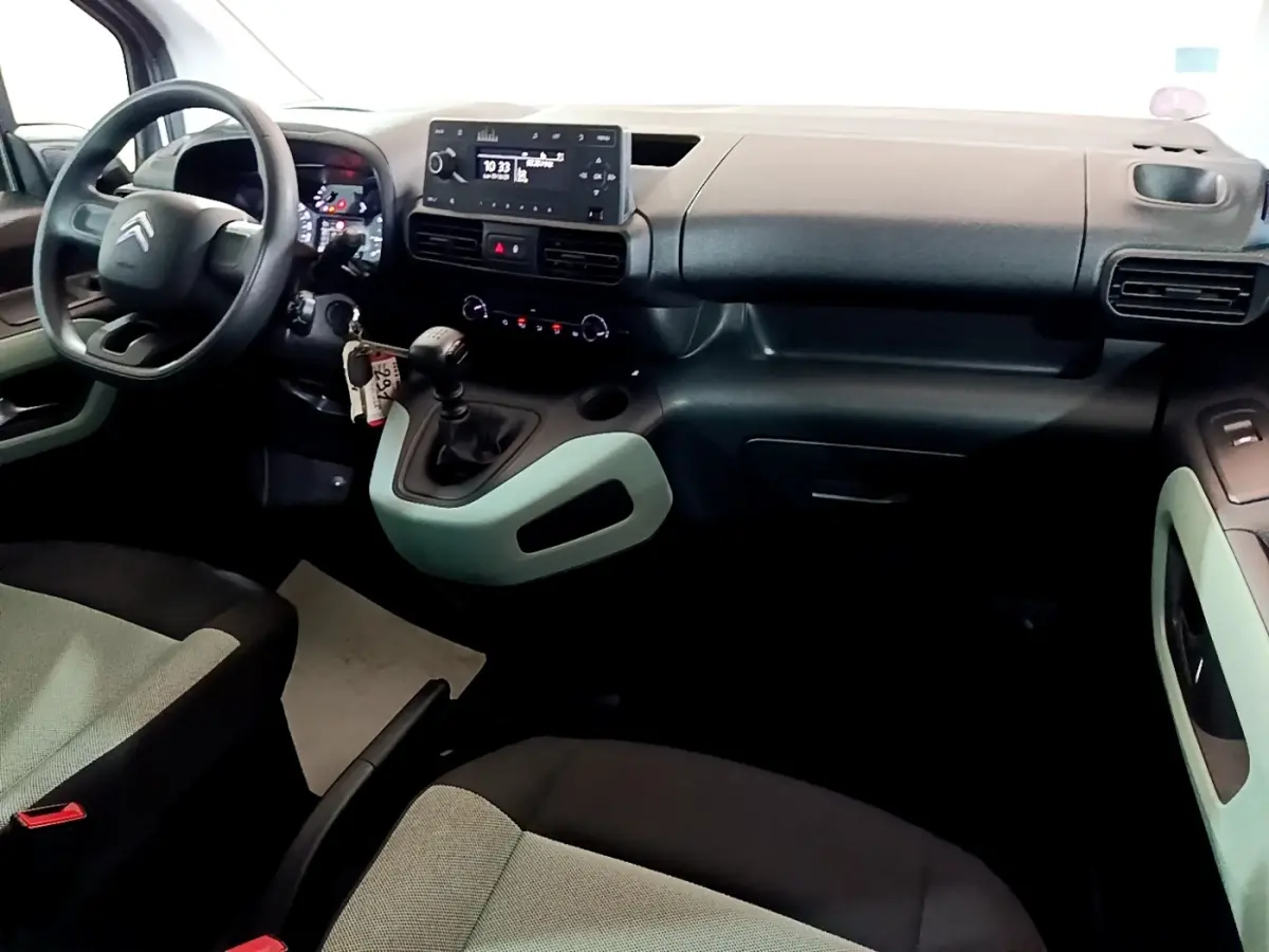 Vue intérieure côté conducteur du Citroën Berlingo XL blanc, montrant le tableau de bord et la console centrale avec boîte manuelle.