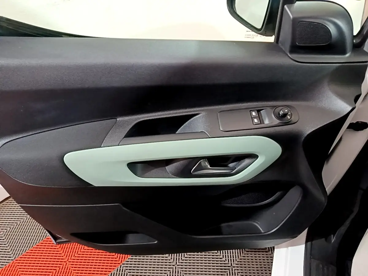 Vue intérieure du panneau de porte avant gauche du Citroën Berlingo blanc, avec poignée et commandes de vitres.