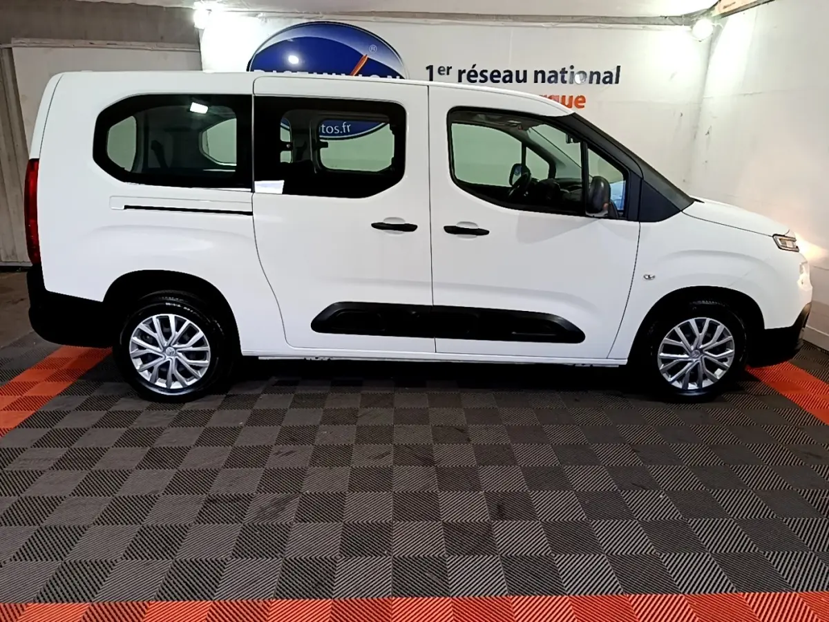 Vue de profil côté gauche d'un Citroën Berlingo XL blanc avec protections noires et jantes alliage en intérieur fermé.