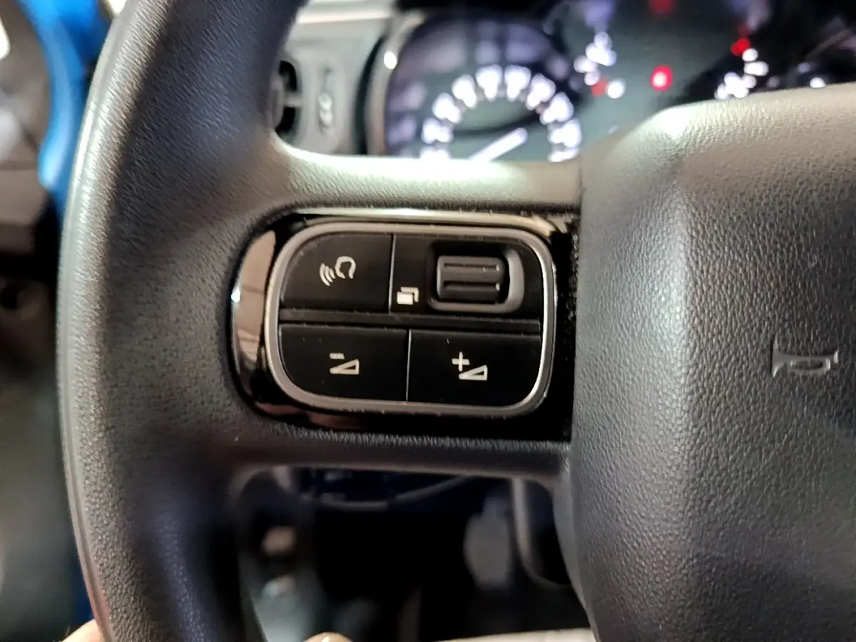 Gros plan sur les commandes au volant noir de la Citroën C3 BlueHDi 2017 avec tableau de bord flou en arrière-plan.