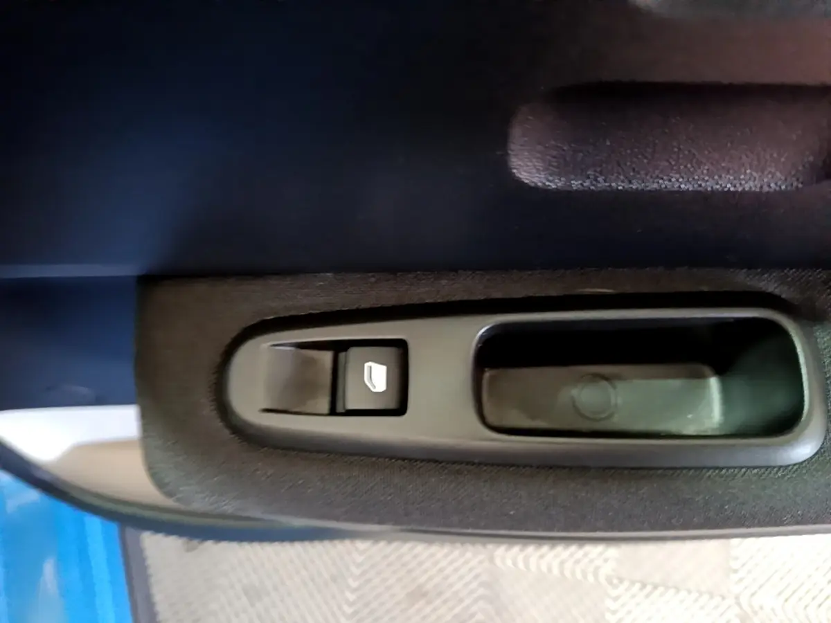 Gros plan sur la commande de lève-vitre côté conducteur d'une Citroën C3 bleu 2017, intérieur tissu noir.