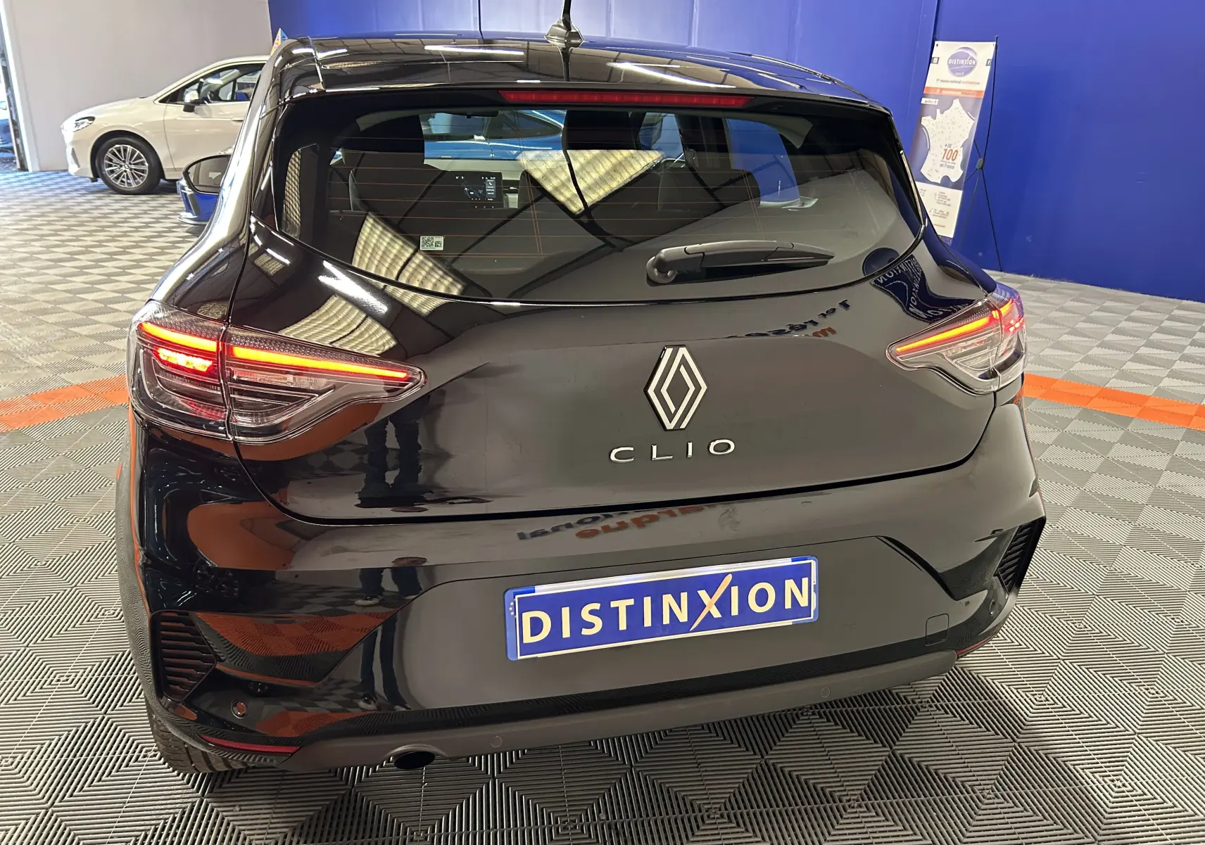 Vue arrière d'une Renault Clio V noire avec feux arrière allumés dans un showroom au sol gris et bleu.
