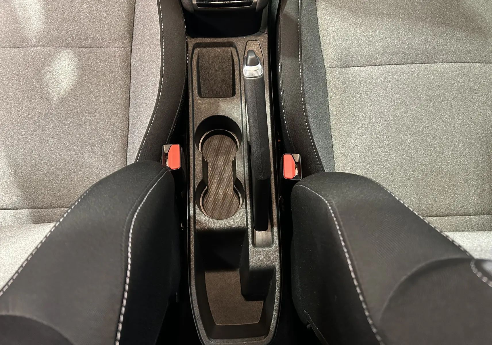 Vue plongeante sur la console centrale noire et les sièges tissu gris de la Renault Clio V Bluetci 100 Evolution.