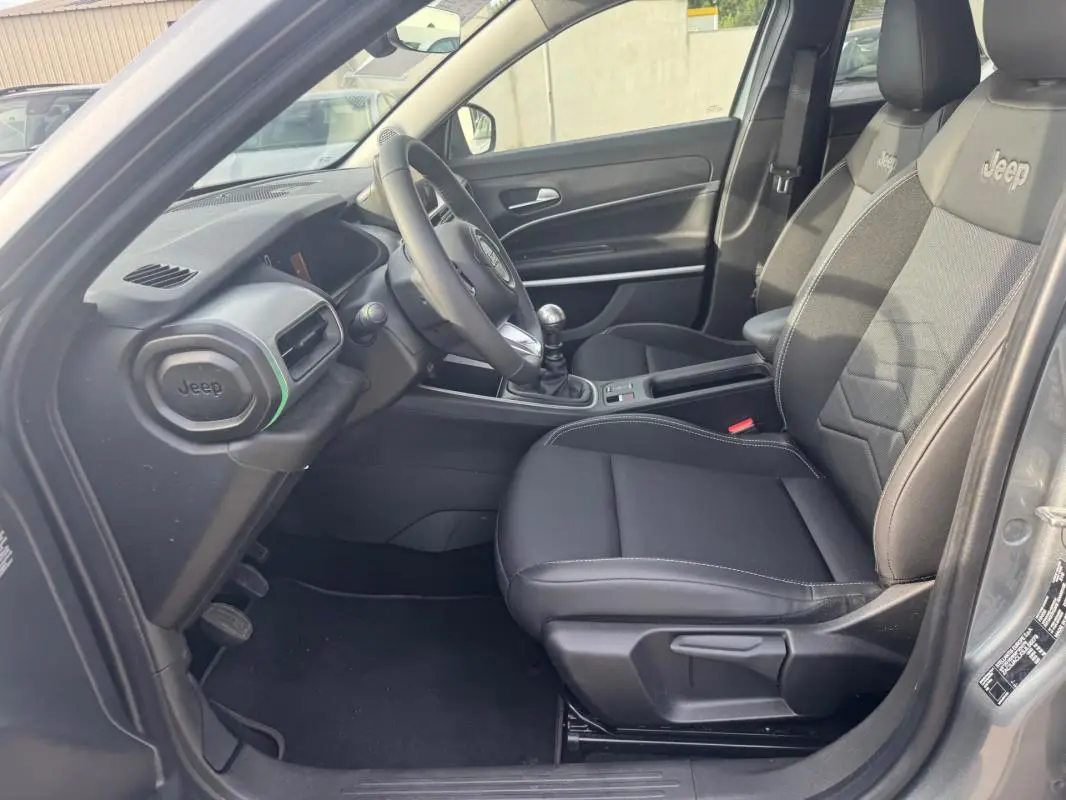 Vue intérieure côté conducteur du Jeep Avenger gris 2025, mettant en valeur les sièges noirs avec logo Jeep et la boîte manuelle.