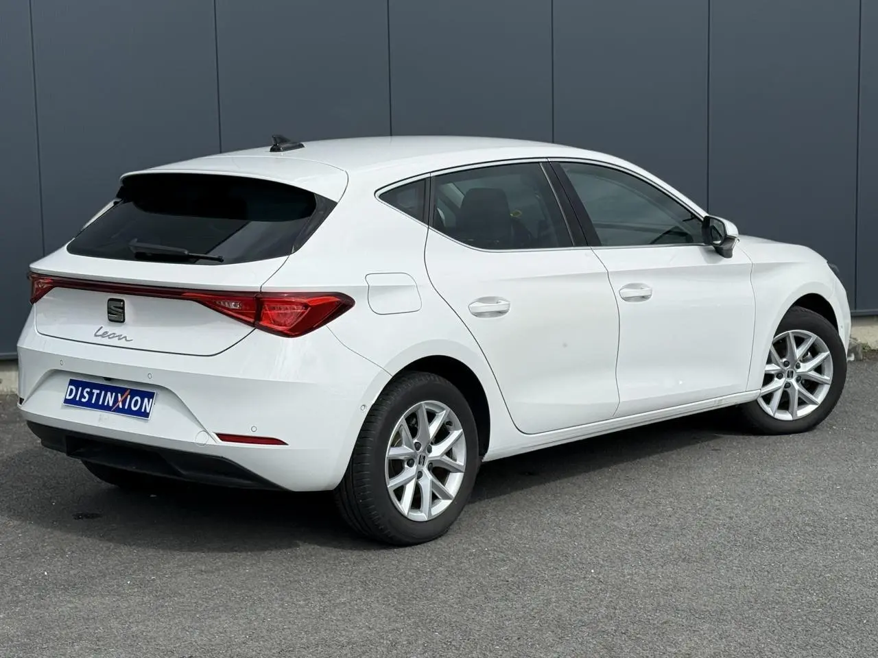 Vue 3/4 arrière droite d'une SEAT Leon blanche avec vitres arrière surteintées et jantes alliage 16 pouces.