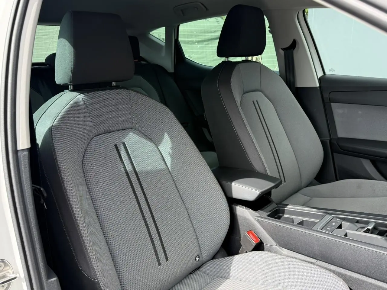Vue intérieure côté avant gauche des sièges tissu gris d’une SEAT LEON blanche avec accoudoir central et console.