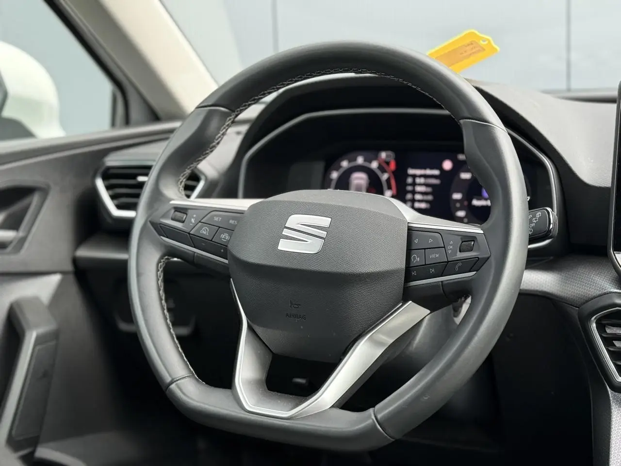 Vue rapprochée du volant cuir multifonction de la SEAT LEON 2025, avec tableau de bord numérique en arrière-plan.