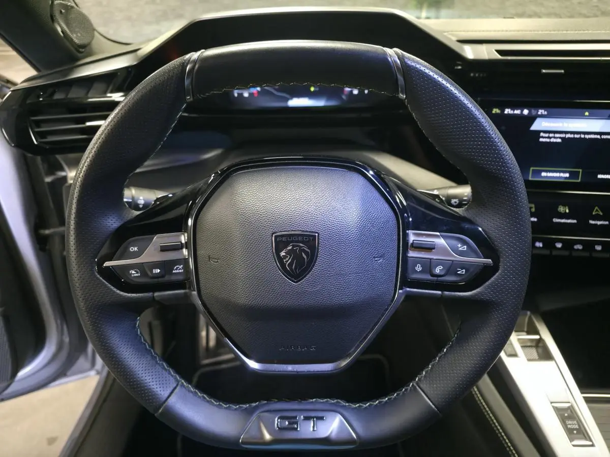 Vue rapprochée du volant cuir noir avec logo Peugeot et badge GT du Peugeot 308 1.6 PHEV 2024.