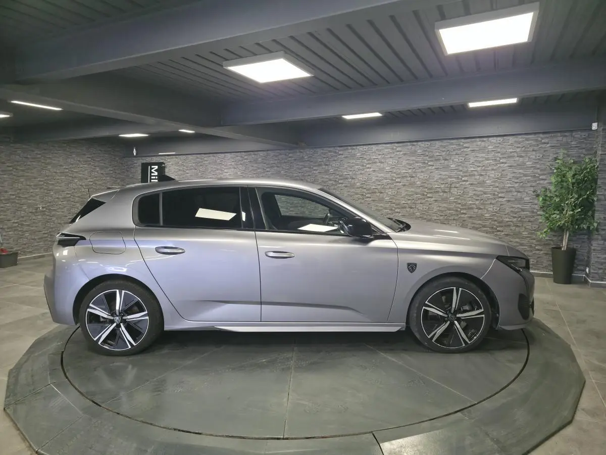 Peugeot 308 gris métallisé vue de profil côté gauche, avec jantes alliage noires et vitres surteintées.