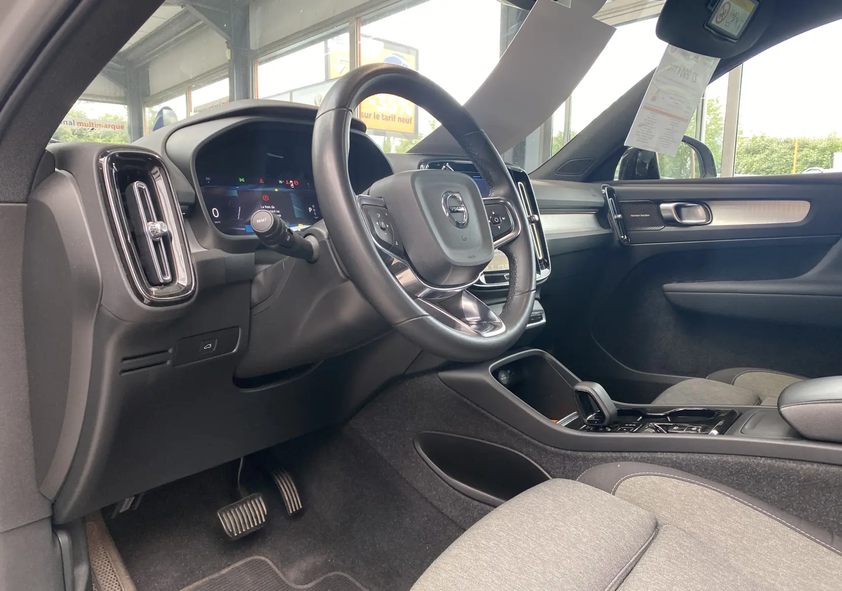 Vue intérieure côté conducteur du Volvo XC40 B3 163ch Plus 2023, volant cuir, tableau de bord numérique et sellerie grise.