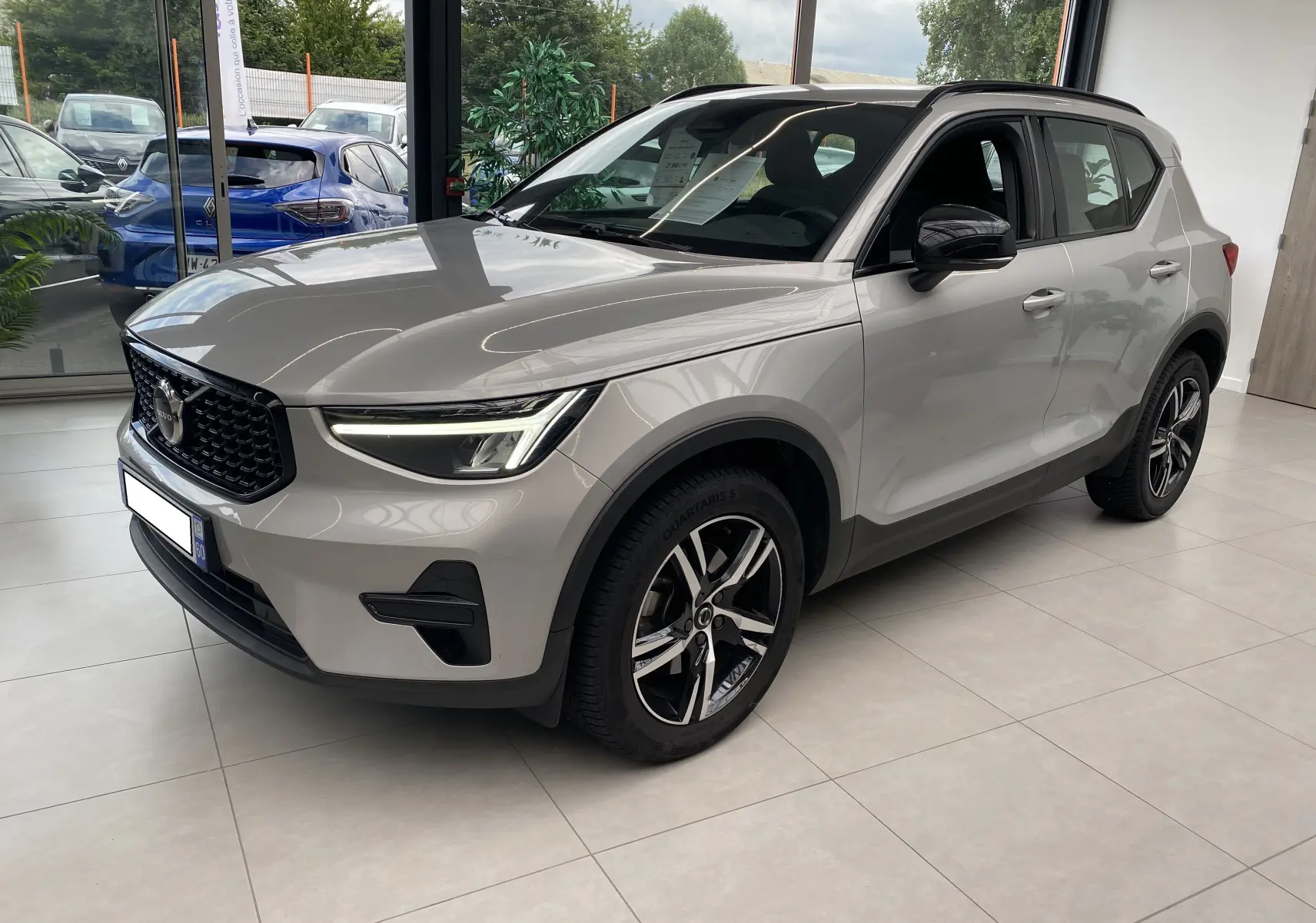 Volvo XC40 B3 argent aurore métallisé en 3/4 avant droit, avec jantes alliage et phares LED allumés en showroom.
