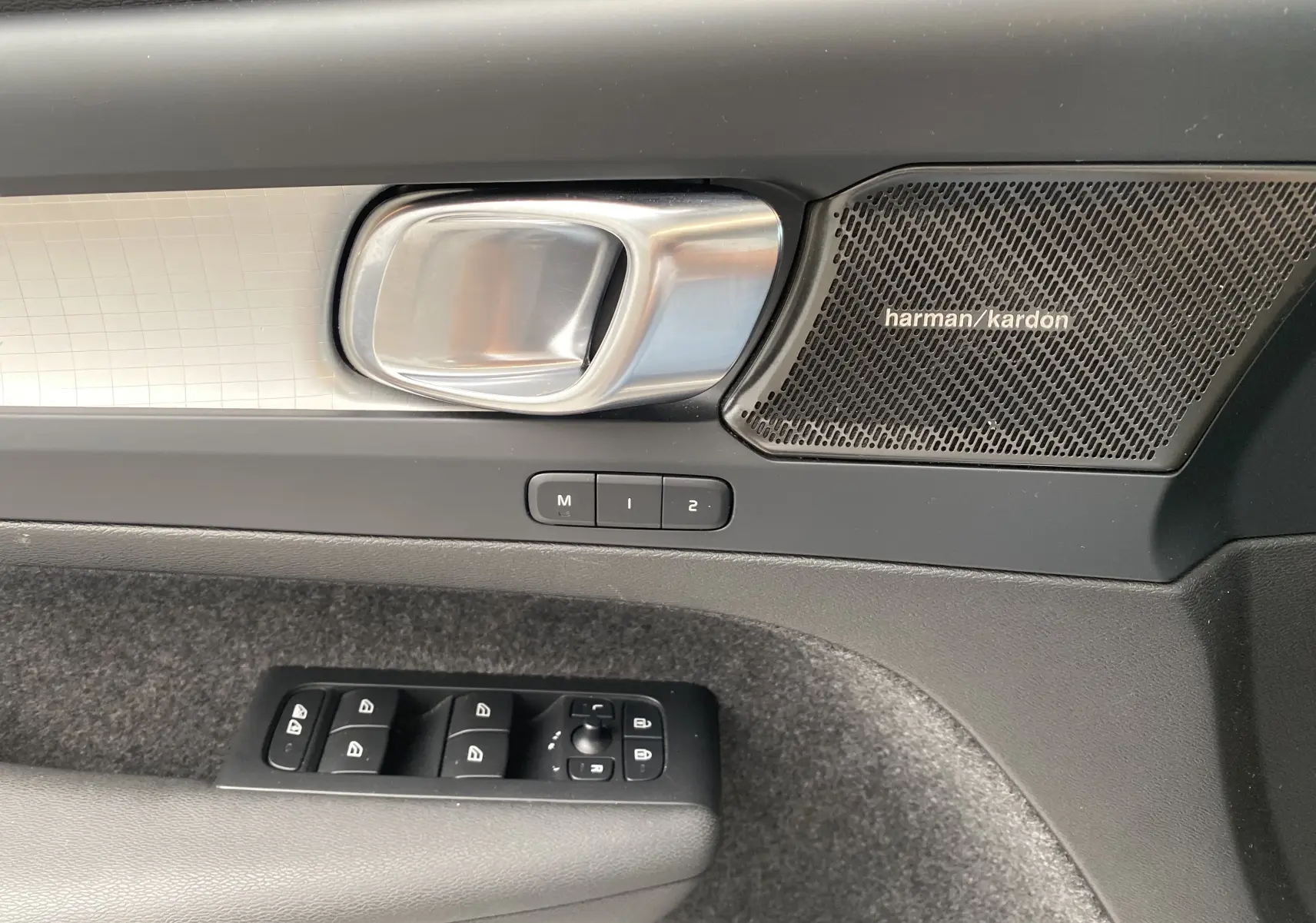 Poignée de porte intérieure côté gauche du Volvo XC40 2023 avec haut-parleur Harman Kardon et commandes des vitres.