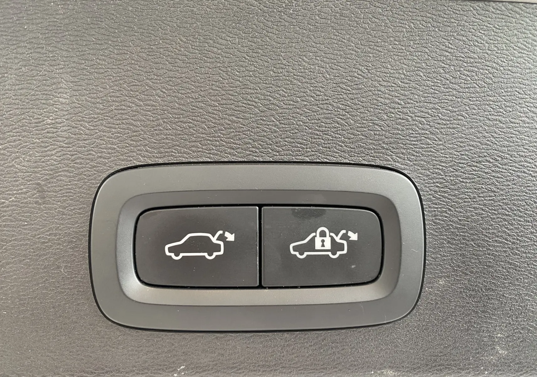 Boutons de commande du coffre avec ouverture et verrouillage sur fond noir texturé, intérieur d'un Volvo XC40 argenté.