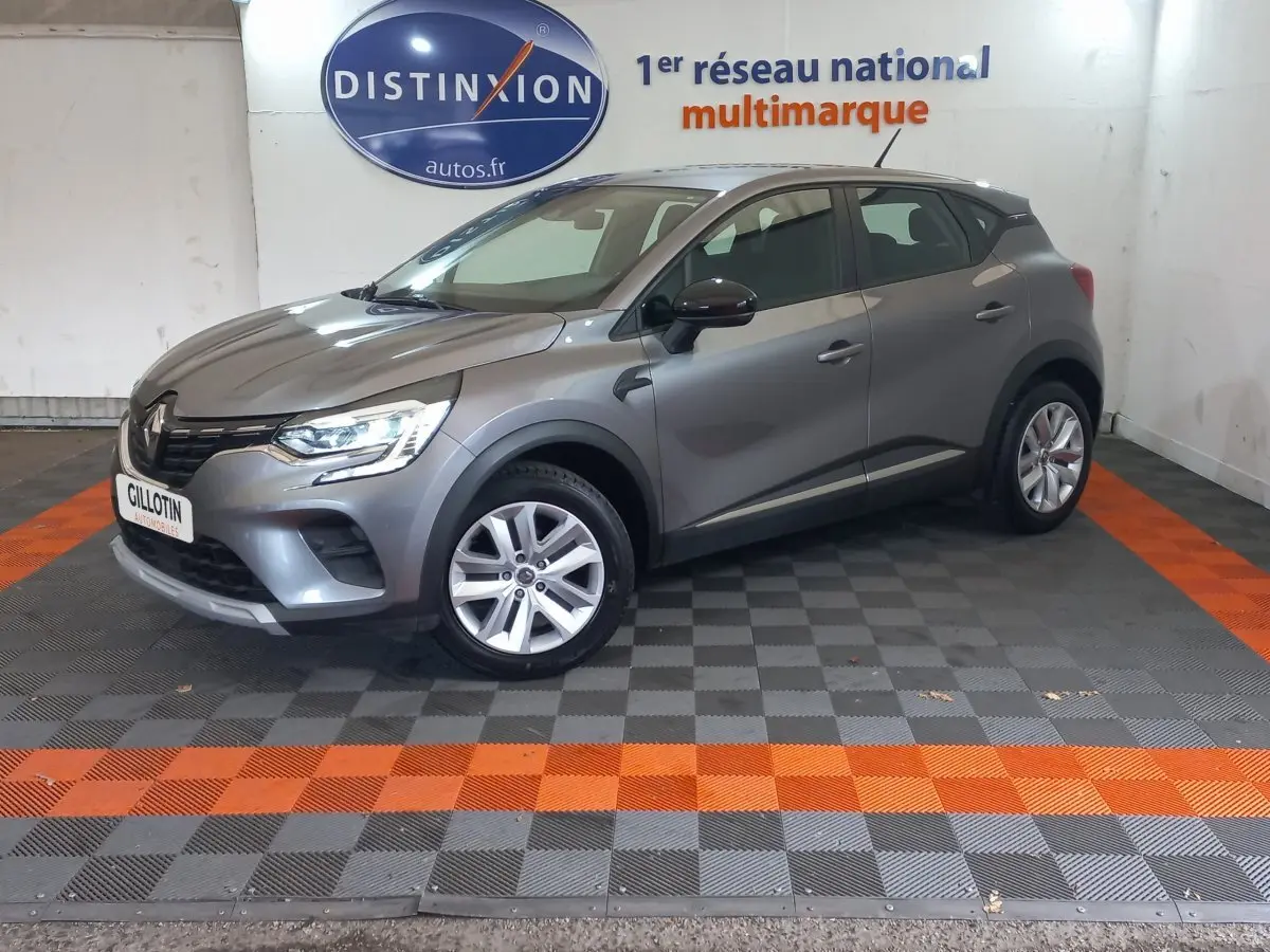 Renault Captur Business TCe 100 gris clair vu de profil côté gauche dans un showroom avec sol gris et orange.