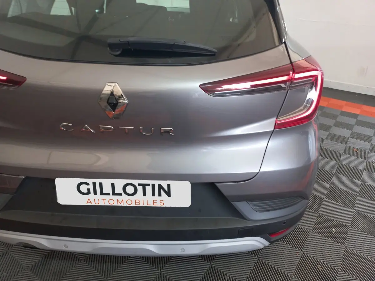 Vue arrière droite d'un Renault Captur gris clair avec feux LED et logo visible sur un sol à motifs.