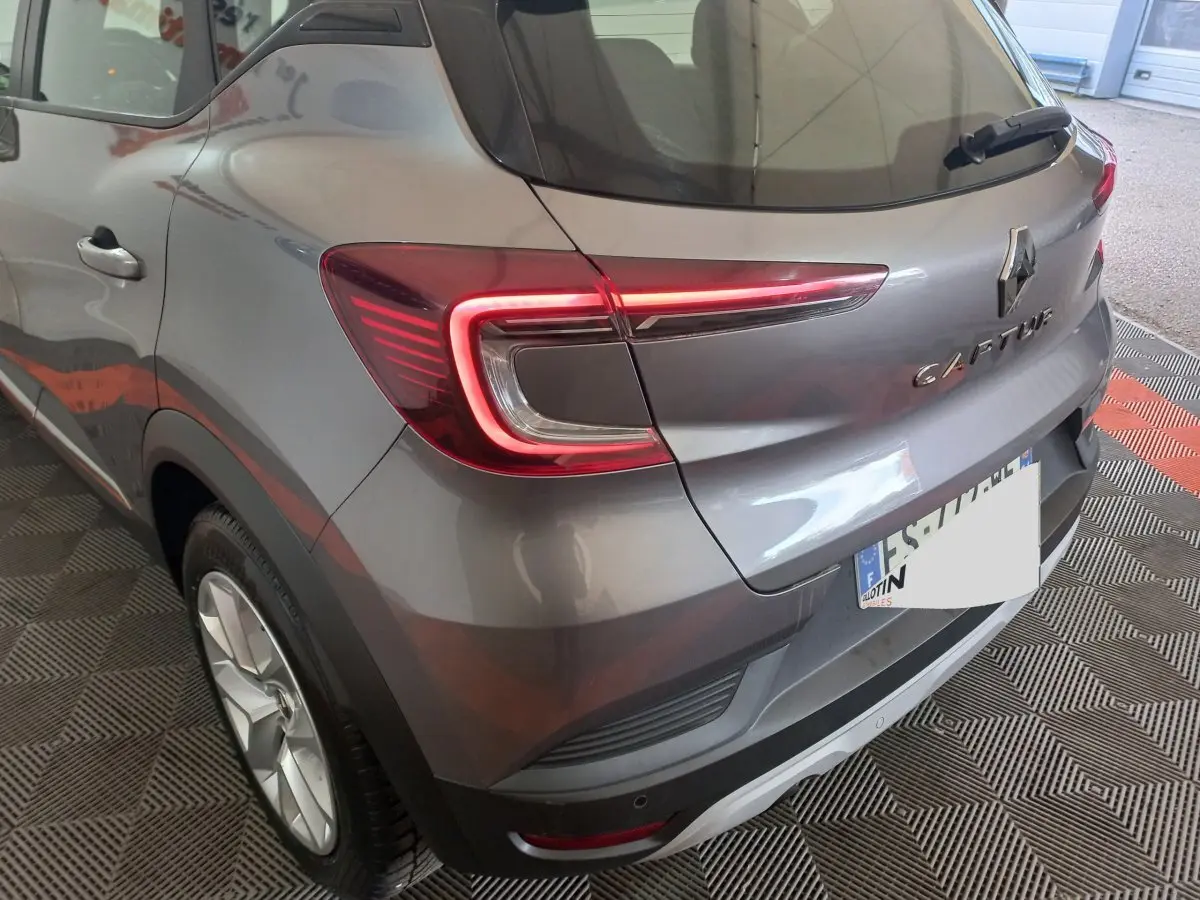 Vue 3/4 arrière droite d'un Renault Captur gris clair avec feux arrière LED et logo visible sur un sol à damiers.