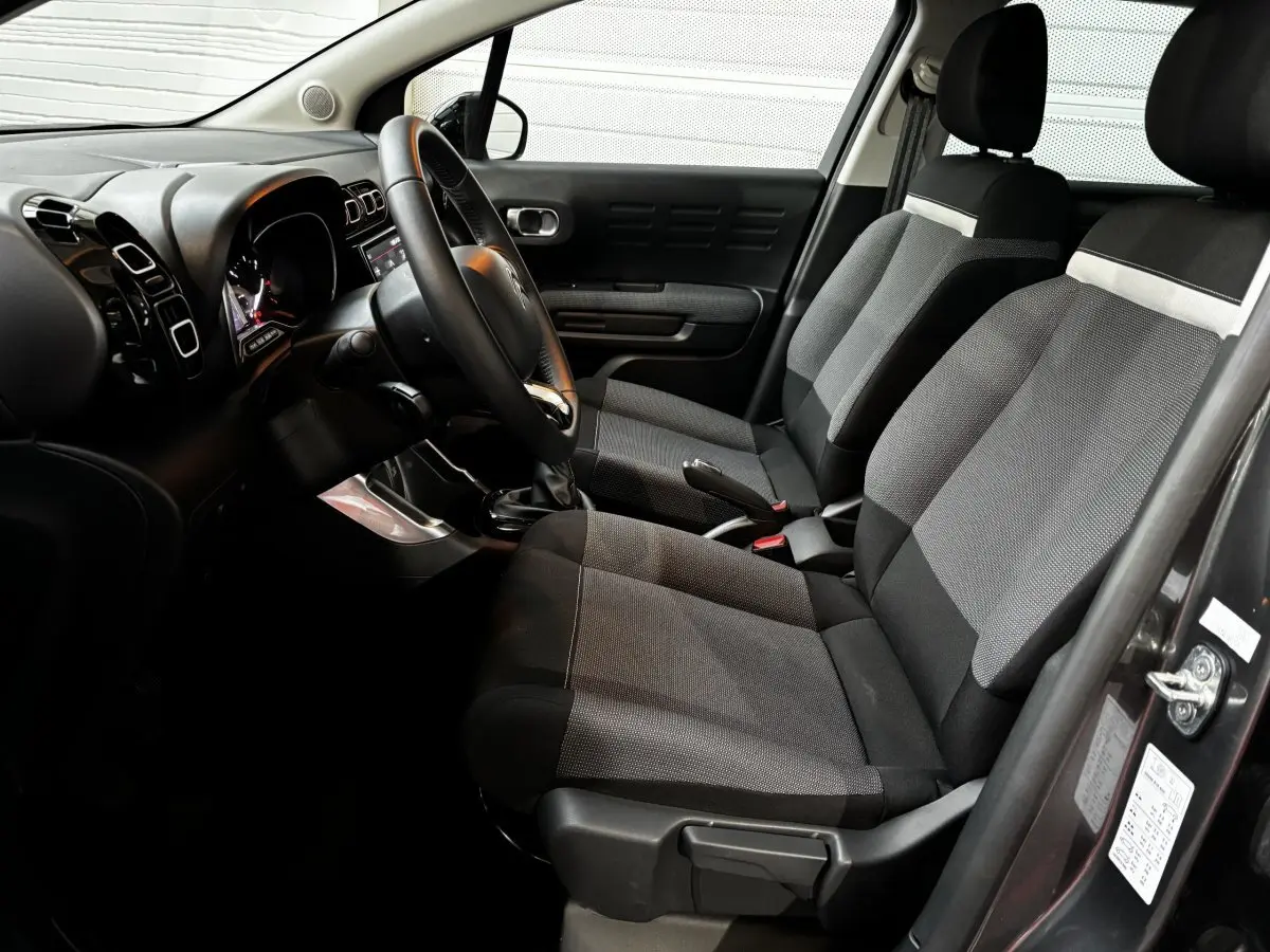 Vue intérieure côté conducteur de la Citroën C3 Aircross gris foncé, sièges tissu bicolore et tableau de bord moderne.