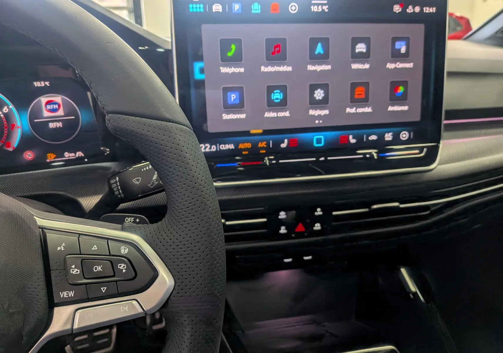 Intérieur de Volkswagen Golf 2025 gris Dauphin, vue du volant et écran tactile central avec commandes digitales.