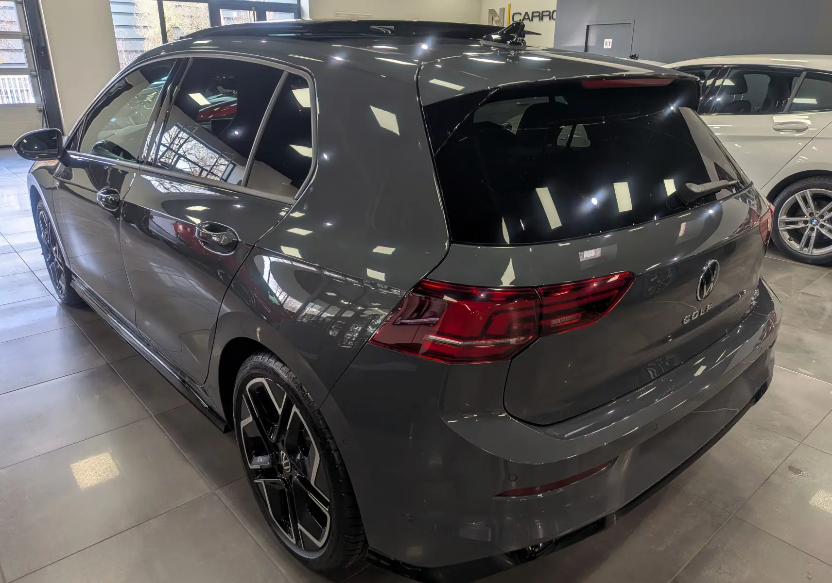 Vue 3/4 arrière droite d'une Volkswagen Golf 1.5 eTSI R-Line gris dauphin avec jantes noires en showroom.