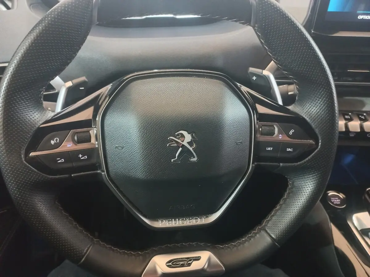 Vue rapprochée du volant cuir noir avec logo Peugeot et badge GT du SUV 3008 gris clair 2022.