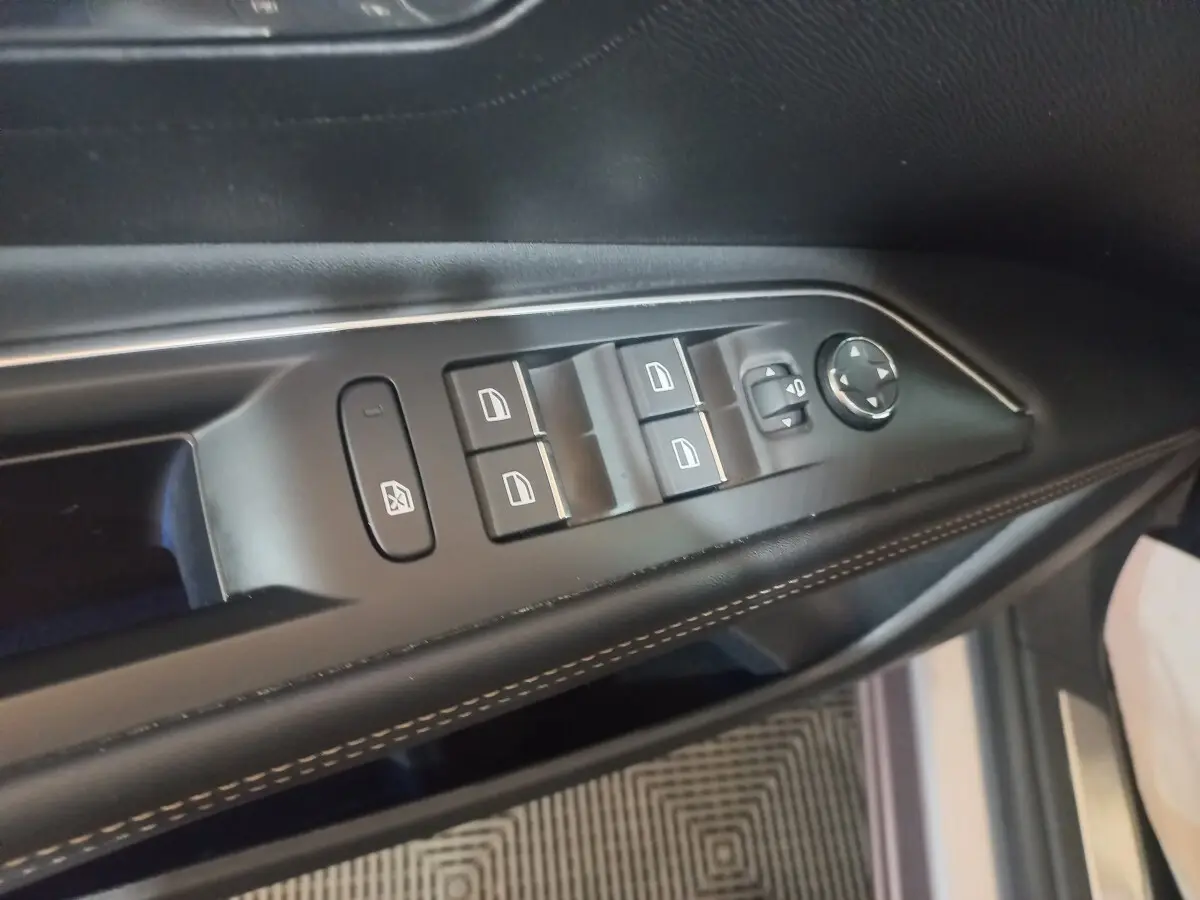 Vue rapprochée des commandes des vitres et rétroviseurs sur la porte côté gauche d’un Peugeot 3008 gris clair.
