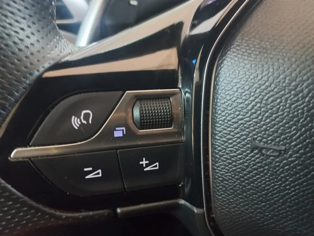 Gros plan sur les commandes vocales et volume du volant cuir noir du Peugeot 3008 PureTech gris clair, version 2022.