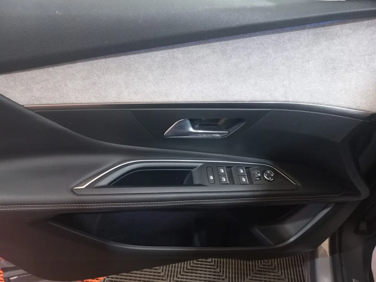 Vue intérieure côté gauche de la porte avant d’un Peugeot 3008 gris clair, avec commandes électriques et poignée chrome.
