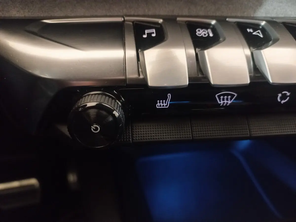 Gros plan sur les commandes argentées et noires du tableau de bord du Peugeot 3008 gris clair, avec éclairage bleu dessous.