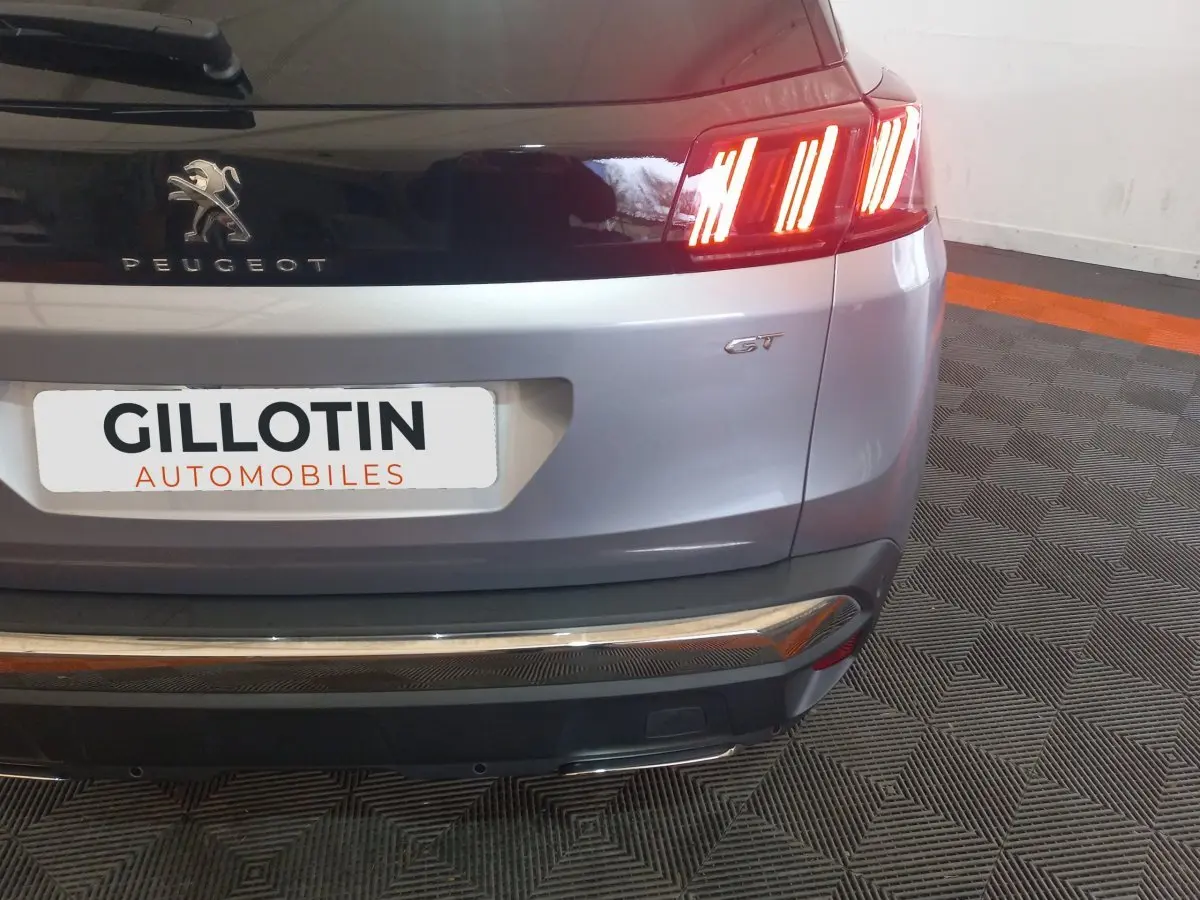 Vue arrière droite du Peugeot 3008 GT gris clair avec feux LED allumés et logo distinctif GT visible.
