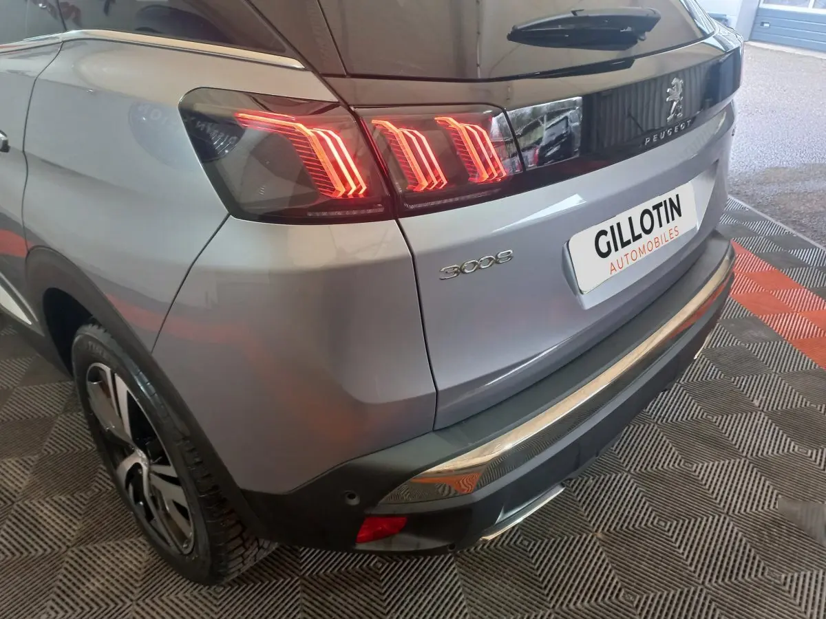 Vue 3/4 arrière droite d’un Peugeot 3008 gris clair avec feux arrière LED allumés et logo visible sur le hayon.