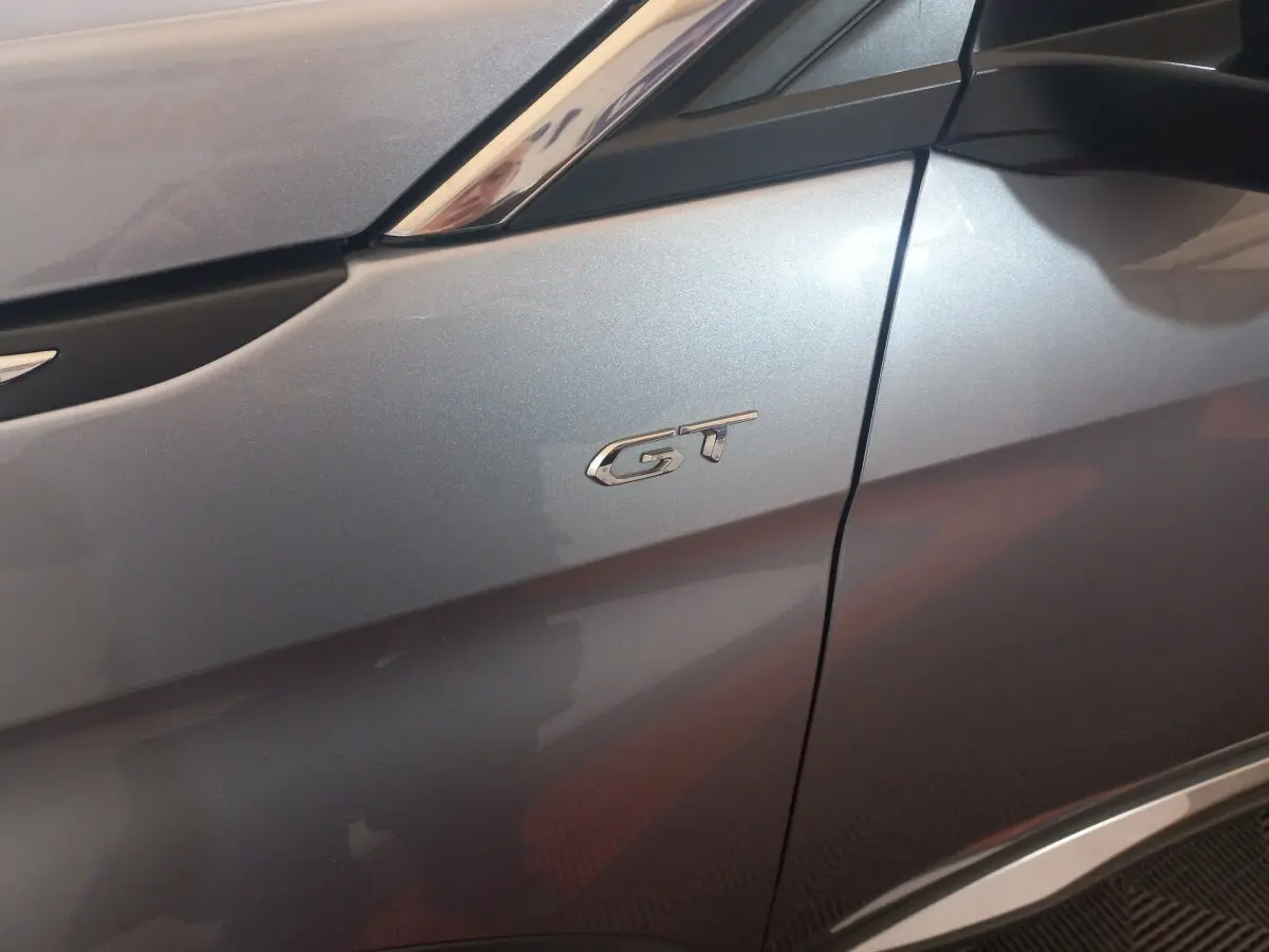Gros plan sur l’aile avant gauche gris clair d’un Peugeot 3008 GT avec logo GT chromé visible.