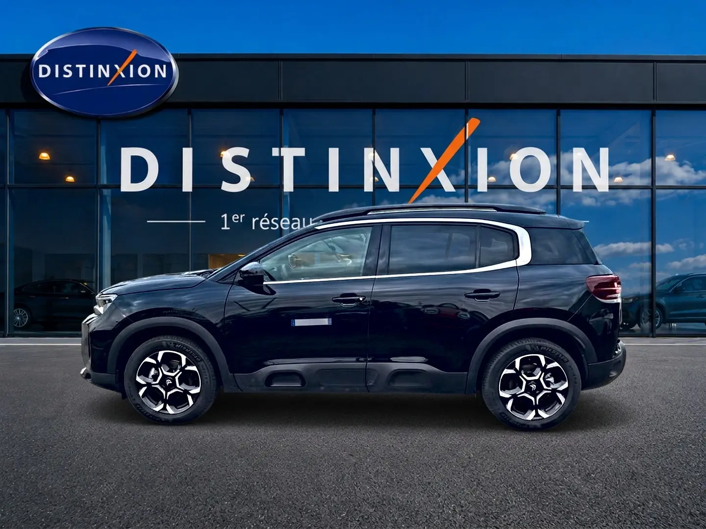 Profil côté gauche d'un Citroën C5 Aircross noir 2025 avec jantes alu et barres de toit visibles devant une vitrine Distinxion.