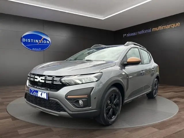 Vue 3/4 avant droite d'une Dacia Sandero Stepway TCE 110 Extreme Plus gris urban avec jantes noires et barres de toit.