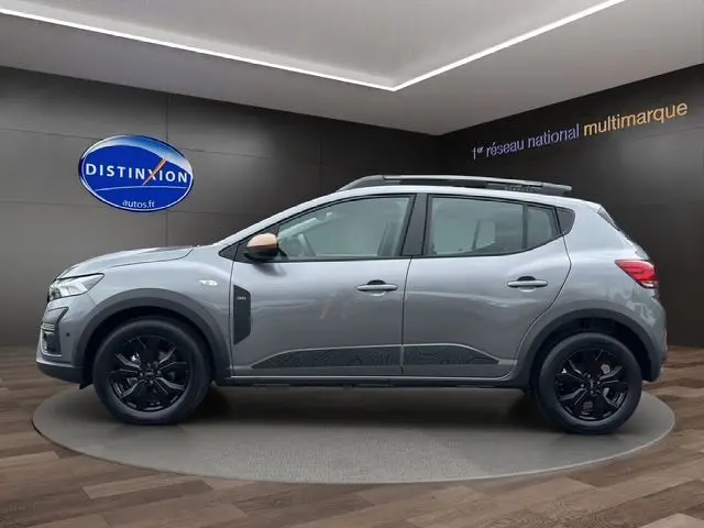 Profil latéral droit d'une Dacia Sandero Stepway TCE 110 Extreme Plus gris Urban avec jantes alu noires et barres de toit noires.