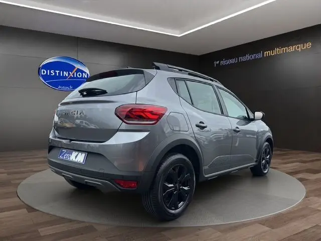 Vue 3/4 arrière droite d'une Dacia Sandero Stepway TCe 110 Extreme Plus gris Urban avec jantes alu noires et barres de toit noires.