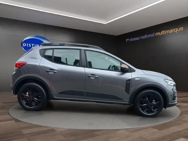 Profil droit de la Dacia Sandero Stepway TCE 110 Extreme Plus gris Urban avec jantes alu noires et barres de toit noires