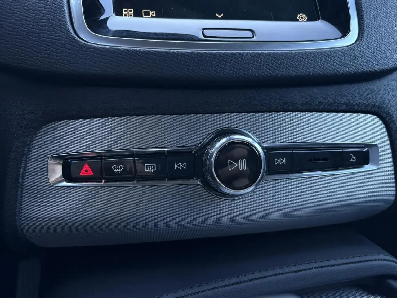 Détail de la console centrale grise du Volvo XC90 2024 avec commandes multimédia et bouton de signalisation lumineux rouge.