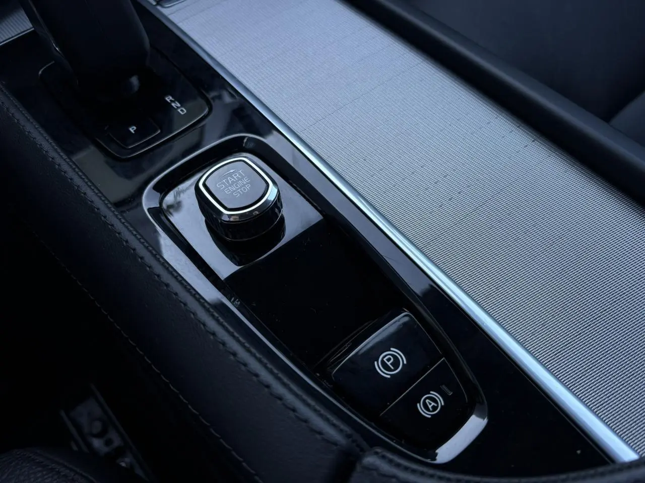 Gros plan sur la console centrale noire du Volvo XC90 2024, avec bouton Start/Stop et frein à main électronique.