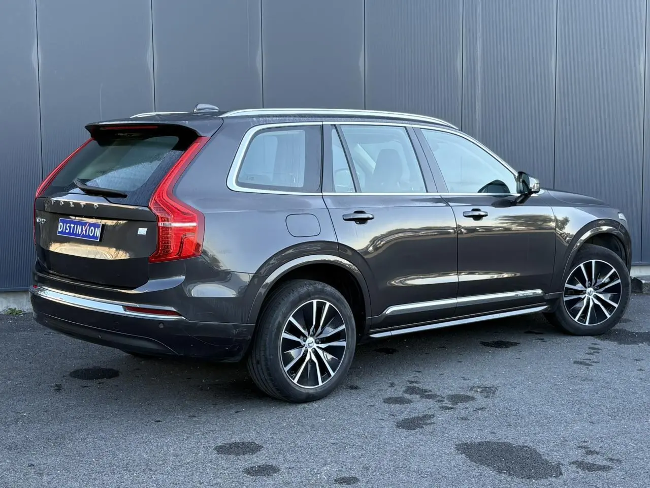 Volvo XC90 T8 hybride gris Platinium vu de 3/4 arrière droit avec jantes alliage noires et chrome aux vitres.