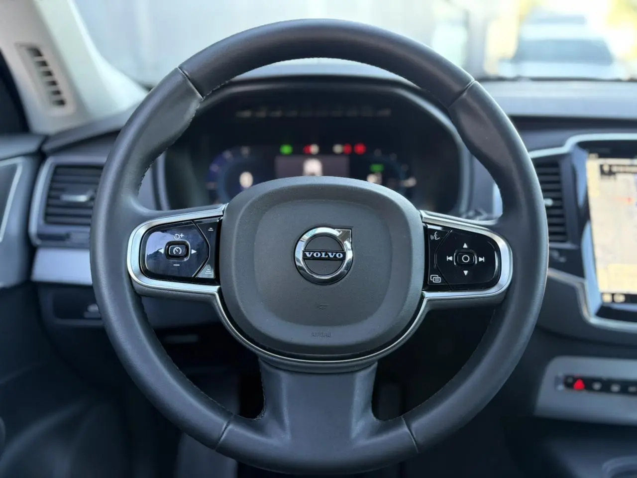 Volant noir de Volvo XC90 T8 2024, vue frontale centrée sur commandes et tableau de bord digital.