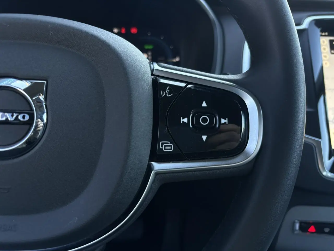Gros plan sur le côté droit du volant noir du Volvo XC90 2024 avec commandes vocales et multimédia intégrées.