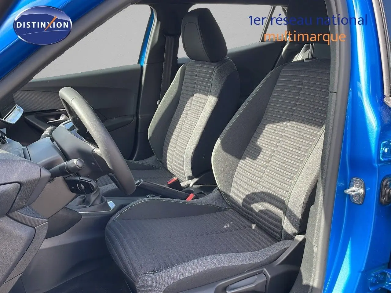 Vue intérieure côté conducteur du Peugeot 2008 2024 bleu Vertigo, sièges tissu noir avec coutures grises visibles.